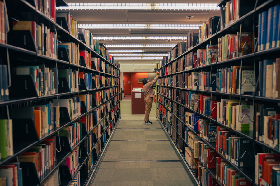 A UP student is at the end of the aisle is taking a book off of the shelf in the Clark Library.