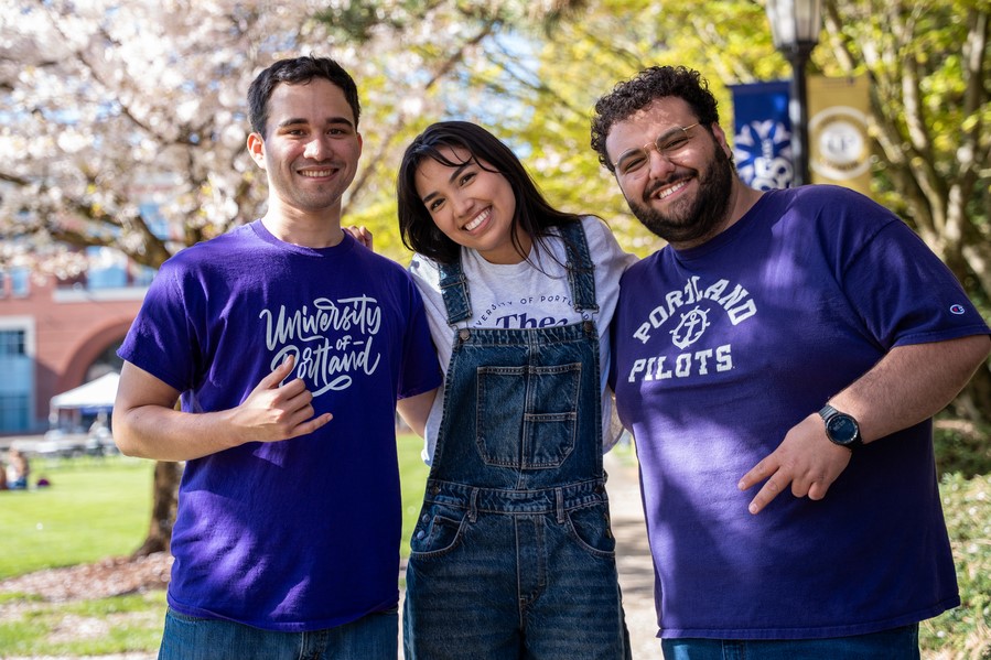 Three UP students link arms and smile for the camera on a sunny day in academic quad.
