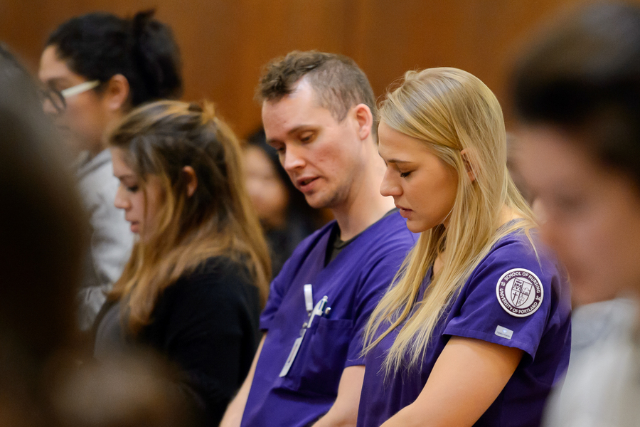 Two University of Portland nursing students stand with heads bowed in a mass of blessing the hands of healthcare workers