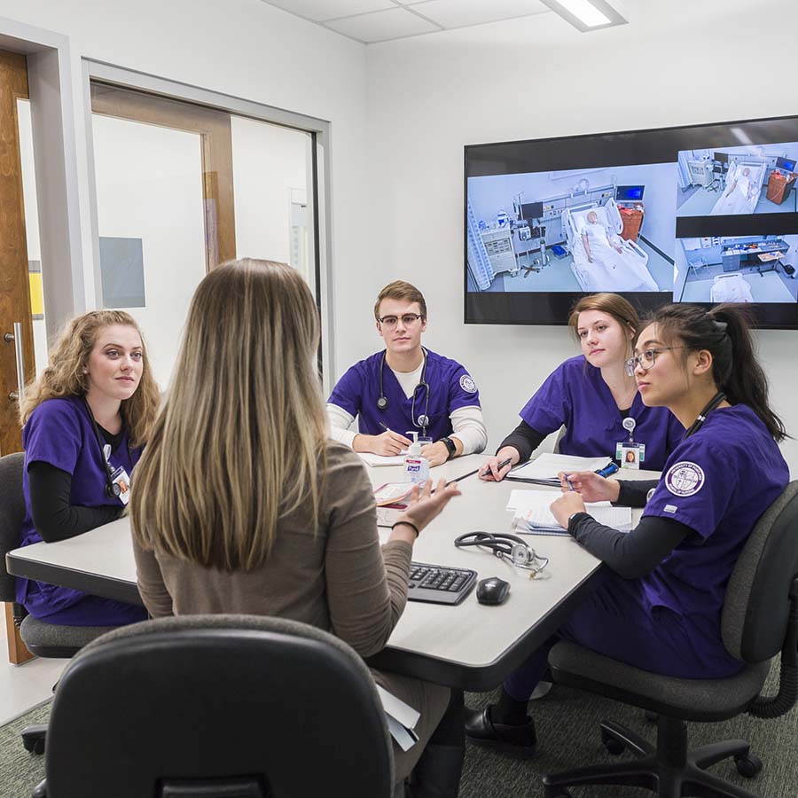 Four University of Portland nursing students in the simulation lab listen intently to their instructor walk them through the essentials of clinical care