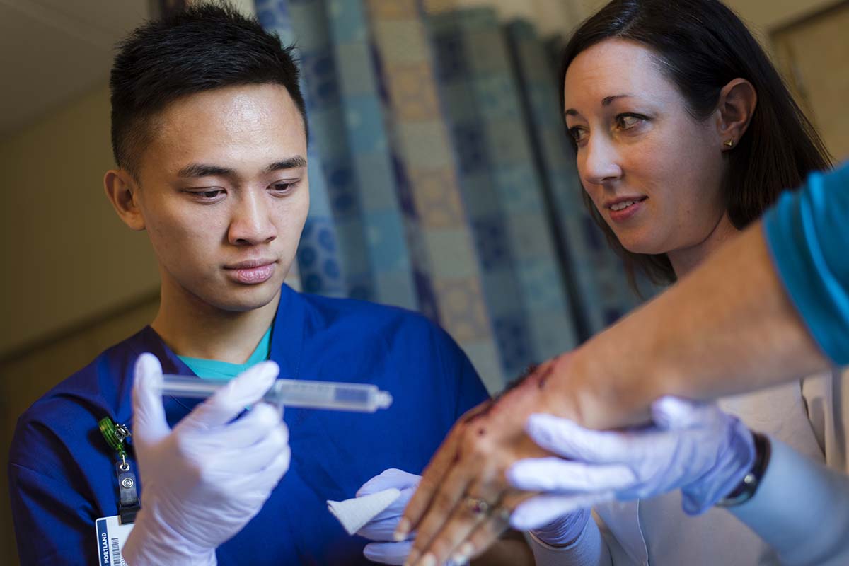 A University of Portland nursing student washes a wound with a saline-filled syringe under instructor supervision in the nursing lab
