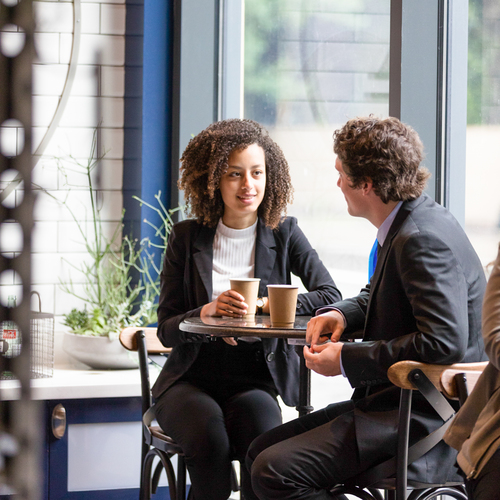 A UP student dressed in professional attire sits with an internship coordinator in the bright daylight of a Portland coffee shop.
