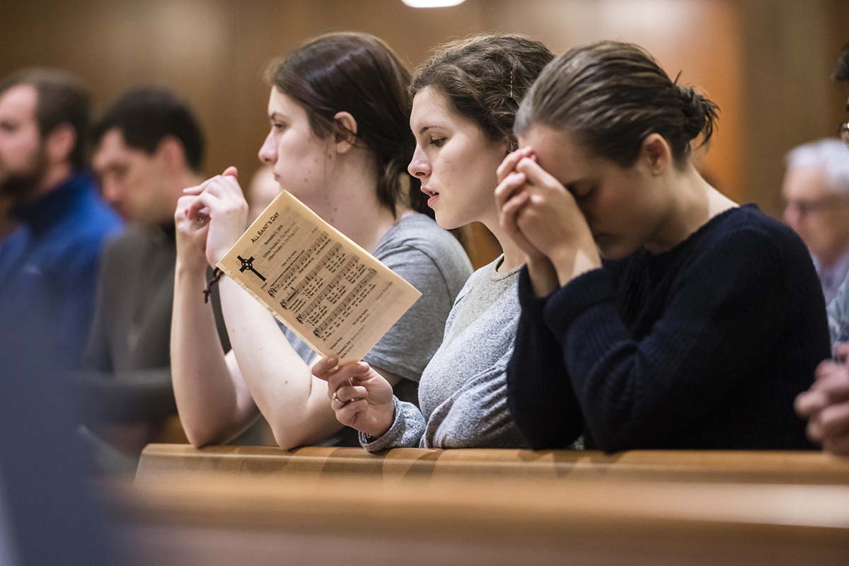 University of Portland students kneel, one holding a booklet of hymns, during the mass of All Saints in the Chapel of Christ the Teacher