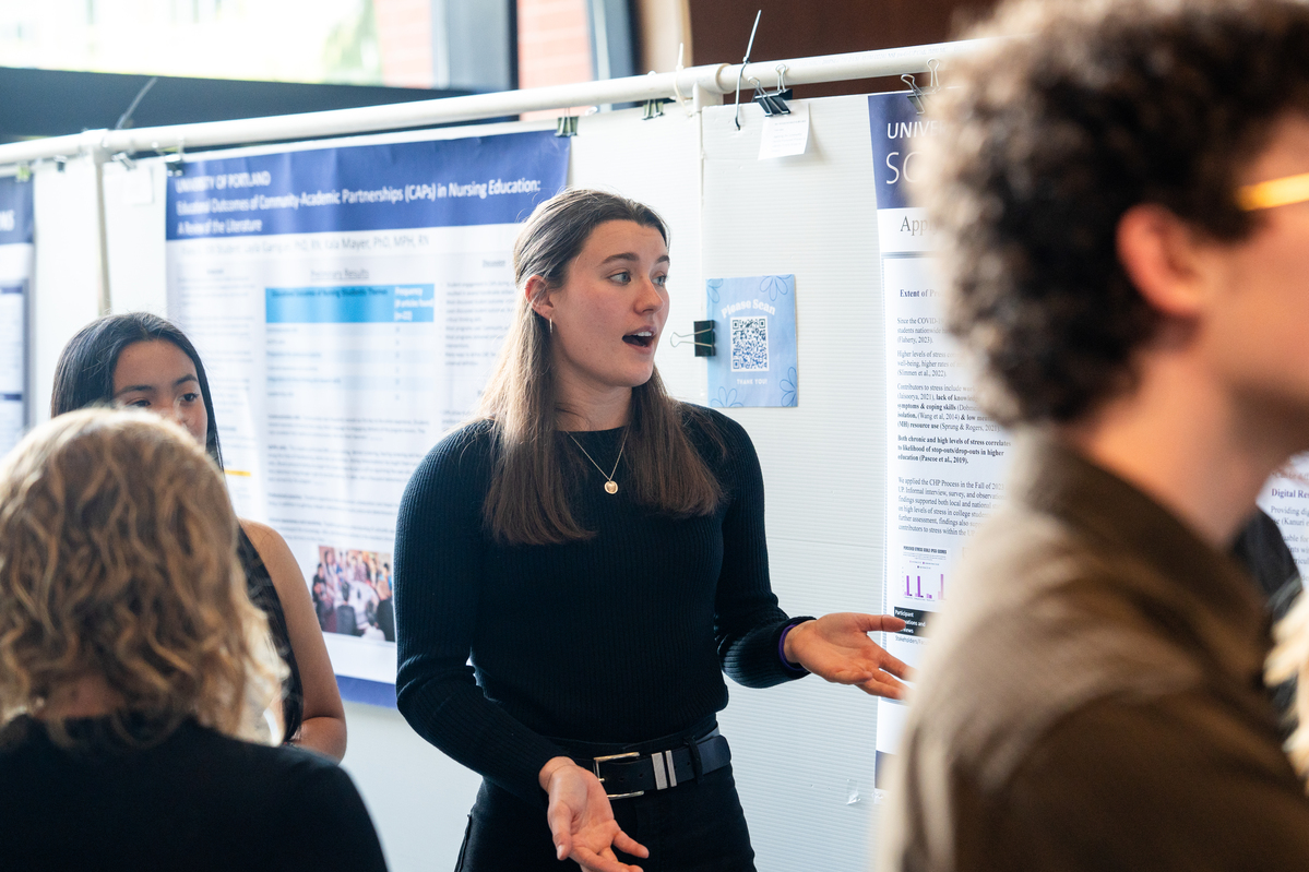 University of Portland student standing in front of a poster of research findings.