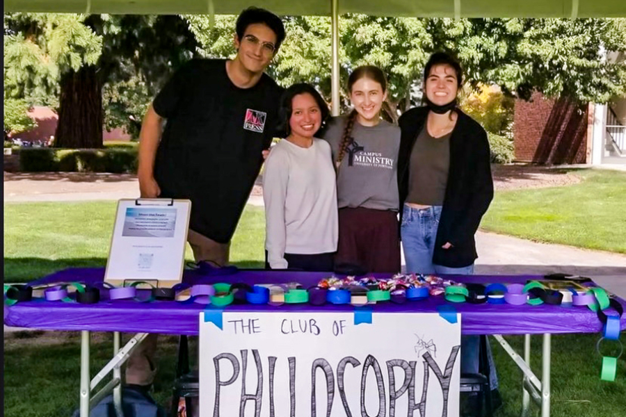 Four students representing the Philosophy Club smile from behind their table at the UP student activity fair on a sunny day outdoors.