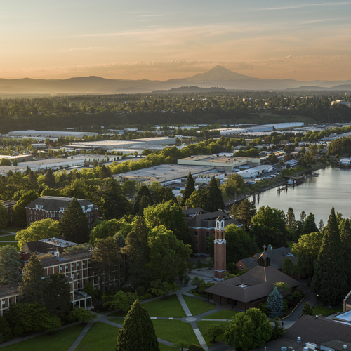 A dramatic aerial view of the University of Portland campus and Mt. Hood set in the backdrop of a rosy hued sunrise.