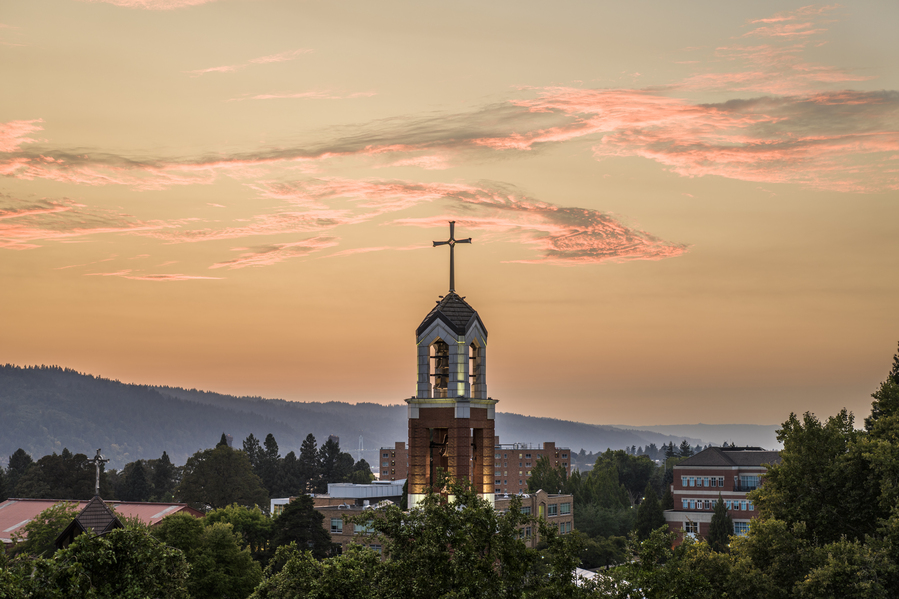An aerial image of the University of Portland bell tower with a glowing pink sunset in the background.