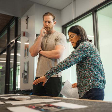 A UP professor reviews a selection of papers on a table with a thoughtful graduate student listening intently.