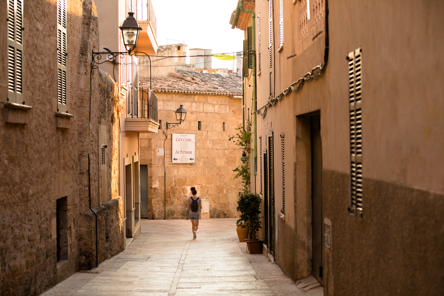 A student walks down a picturesque historic street, paved with stones, in Mallorca, Spain.