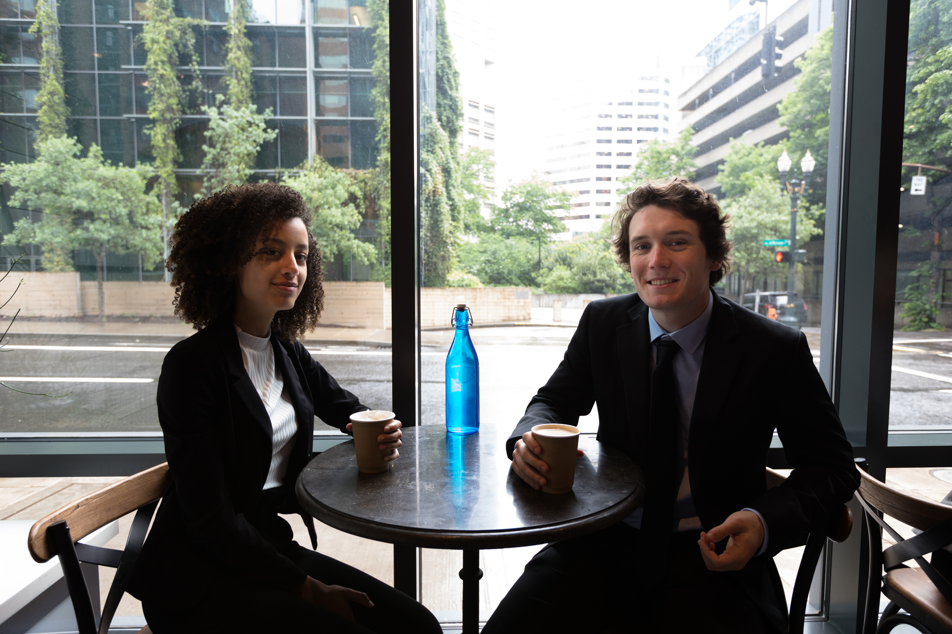 Two University of Portland students sit at a table with coffees in downtown Portland during a break from their internship positions