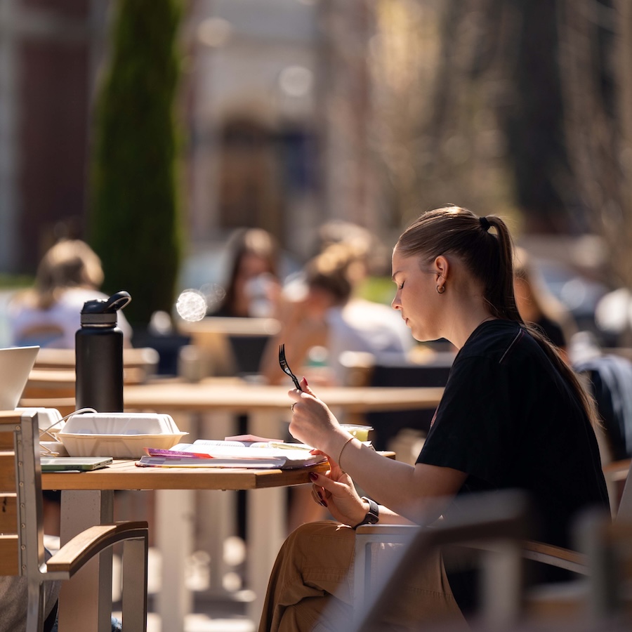 University of Portland student studying at a table outside of the Pilot House in the sunshine