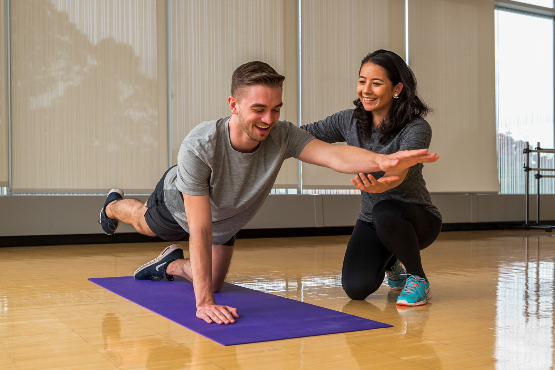 A University of Portland healthcare student guides another student on a bright purple yoga mat in the correct physical movement for health and wellness