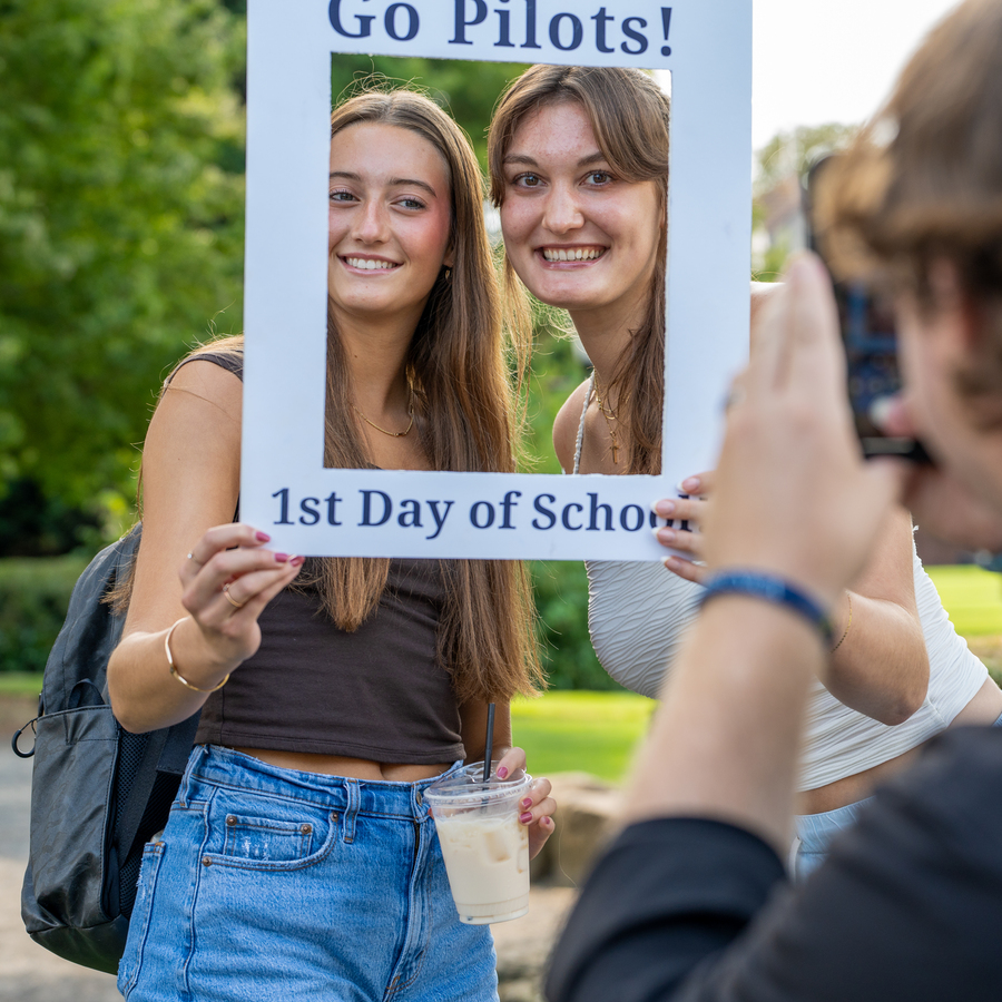 An action shot of a photographer taking a picture of two University of Portland students posing with a paper frame around their faces celebrating the first day of school.