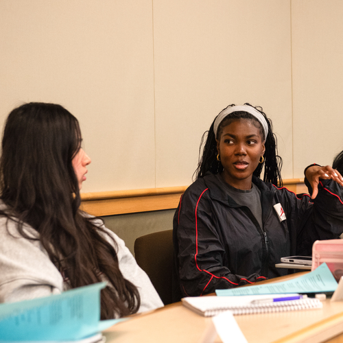 Two students sitting behind a desk discuss course content during an English class at the University of Portland.