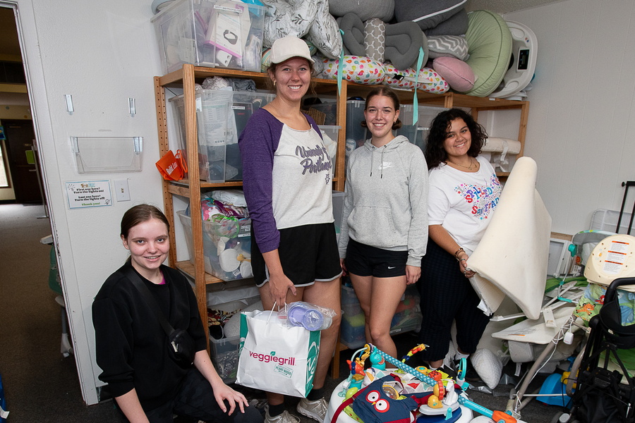 A group of UP students pose with smiles in a room full of donated baby gear as they volunteer for a local charity.
