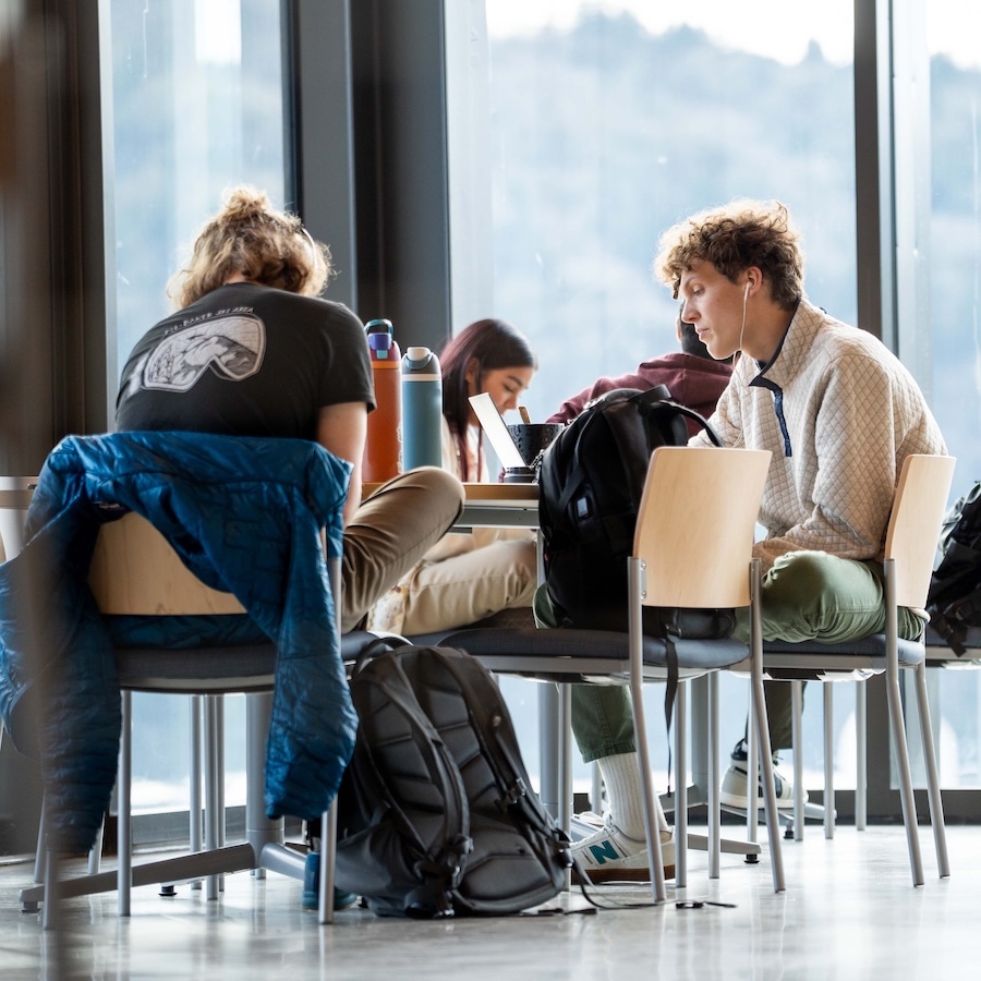 Two University of Portland students studying at a table in front of large windows in the Shiley-Marcos Center for Design and Innovation