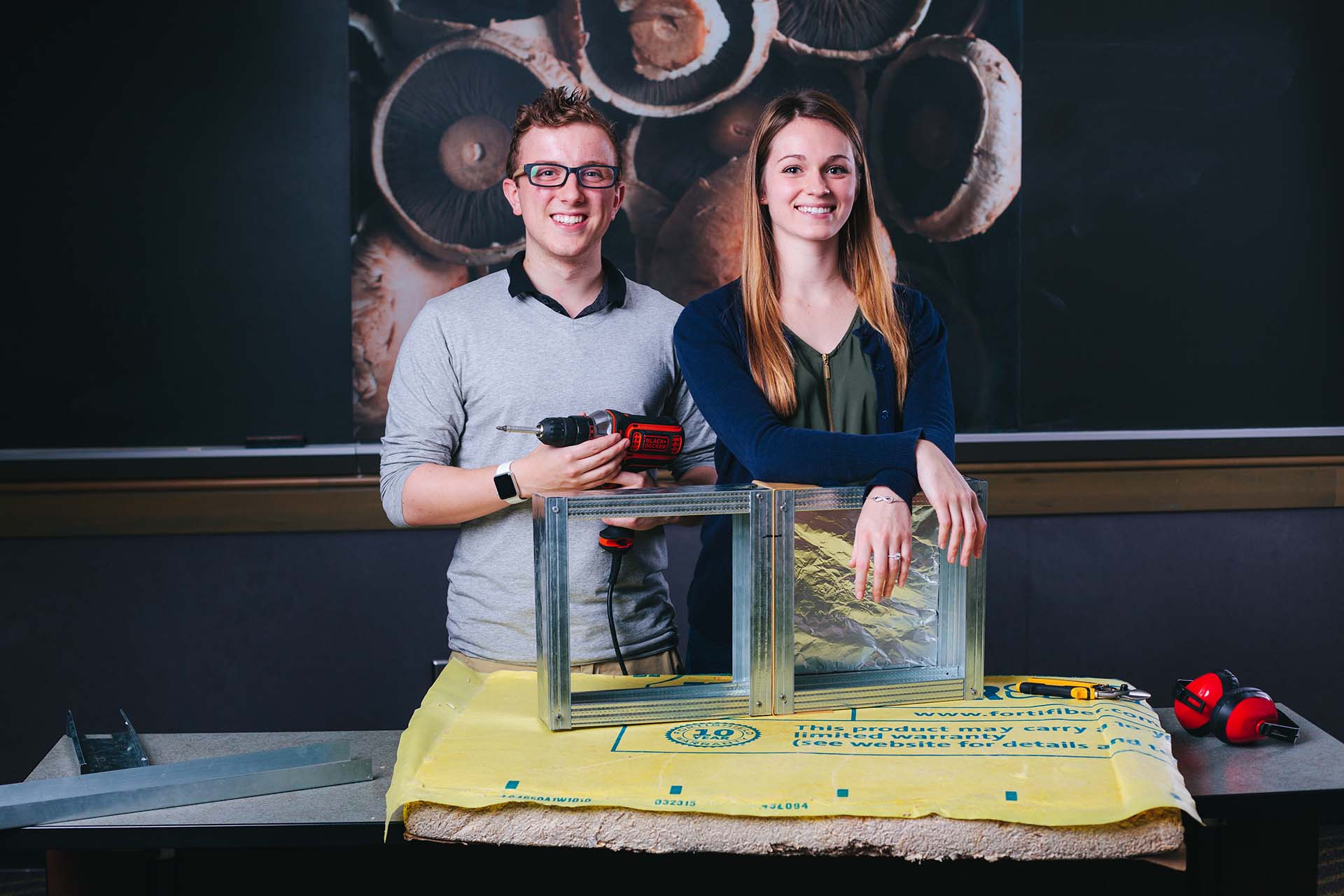 Two University of Portland business students standing with insulation and building products.