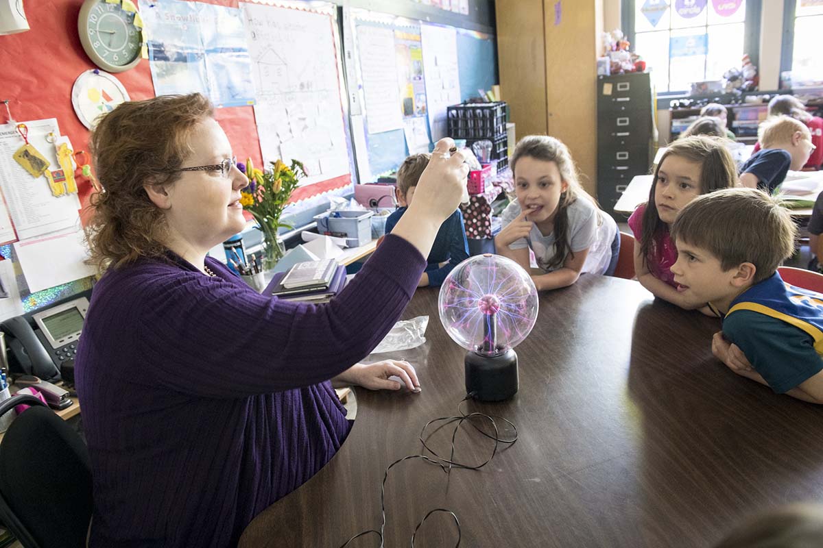 A University of Portland teacher demonstrates a plasma ball to elementary students sitting at a table