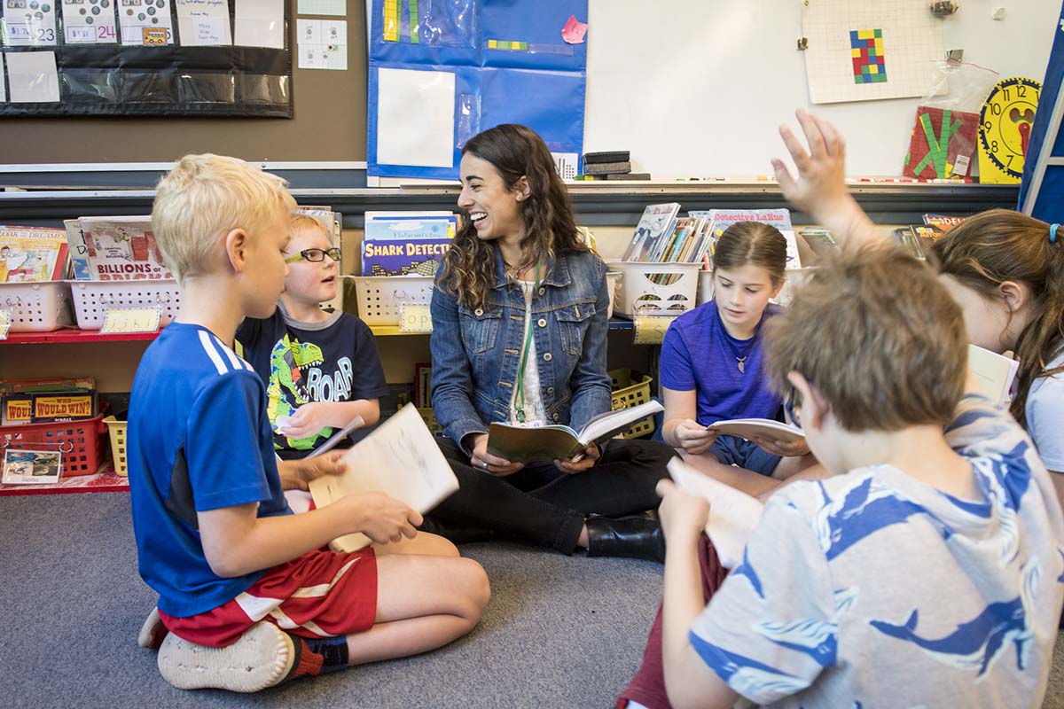 A University of Portland education student teacher sits on the floor with her elementary class reading to them and answering their questions