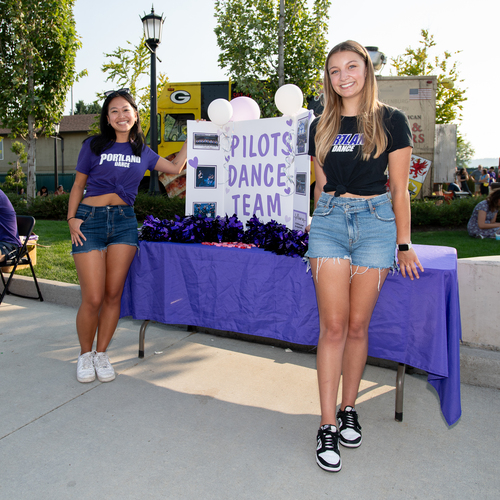 Two students from the University of Portland Dance team pose next to their informational table at the Bite on The Bluff event.