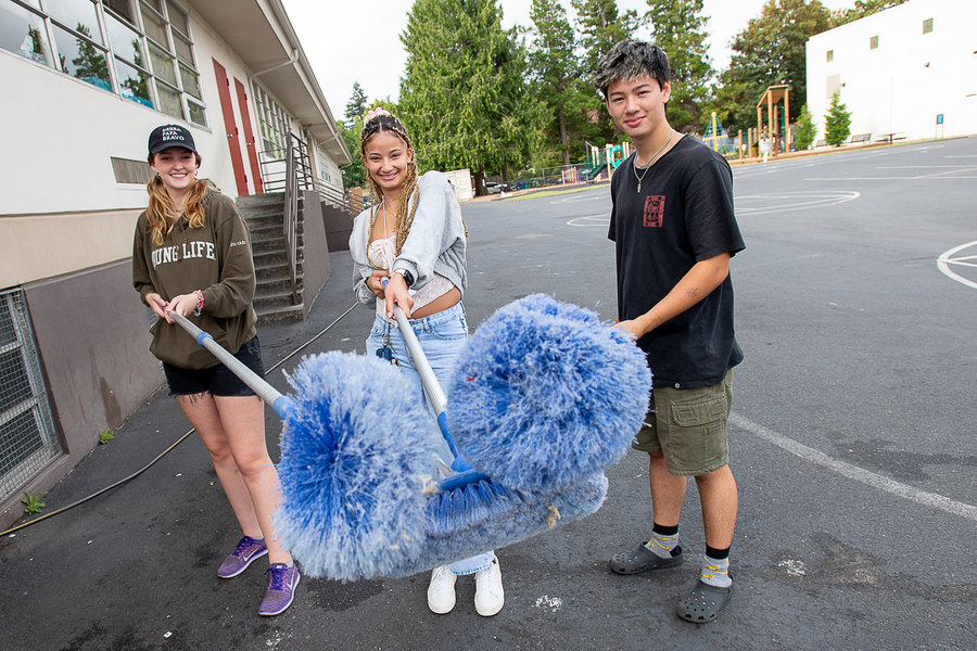 A foreshortened image of three University of Portland students holding their dust brooms up to the camera during the Plunge into Your Neighborhood volunteer event.