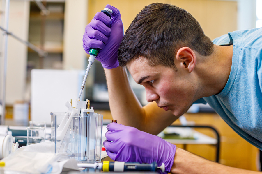 Close-up of a UP chemistry student, looking downward with a focused, serious expression, as they use a pipette in a laboratory setting.