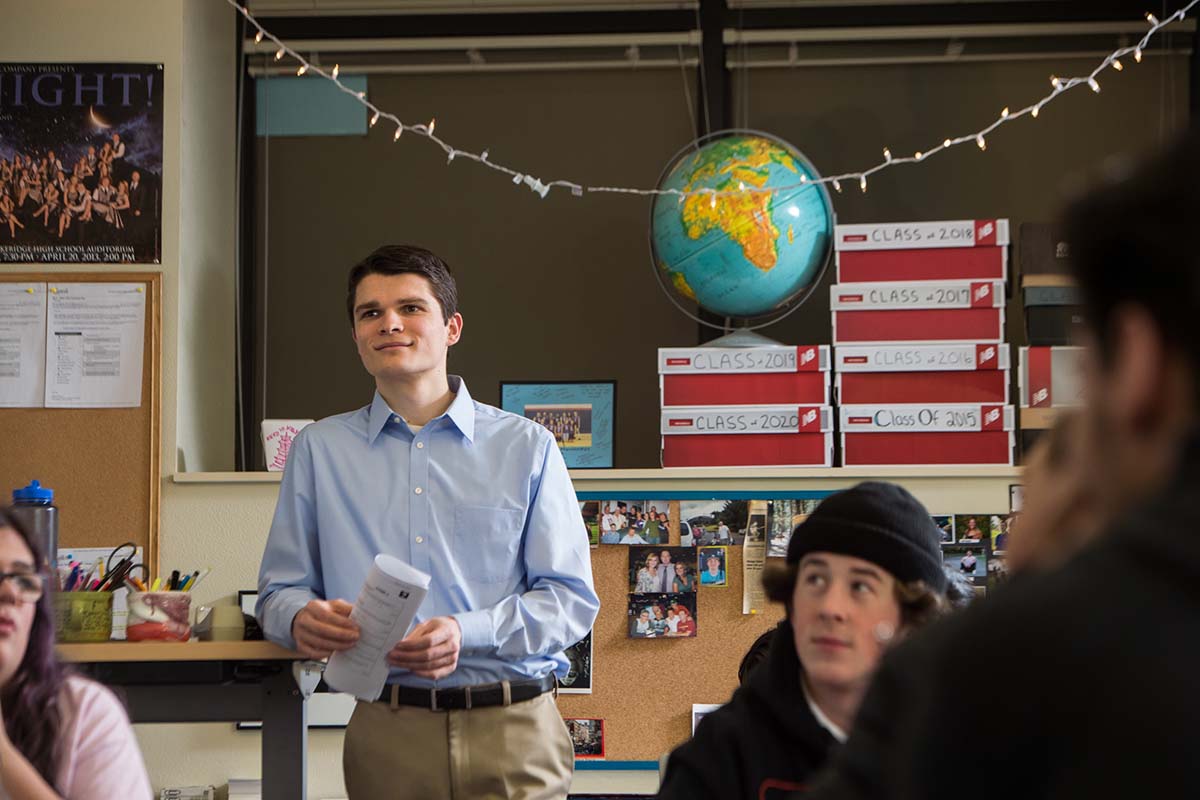 A University of Portland secondary education teaching student stands at the back of class and listens to a student out of sight of the camera