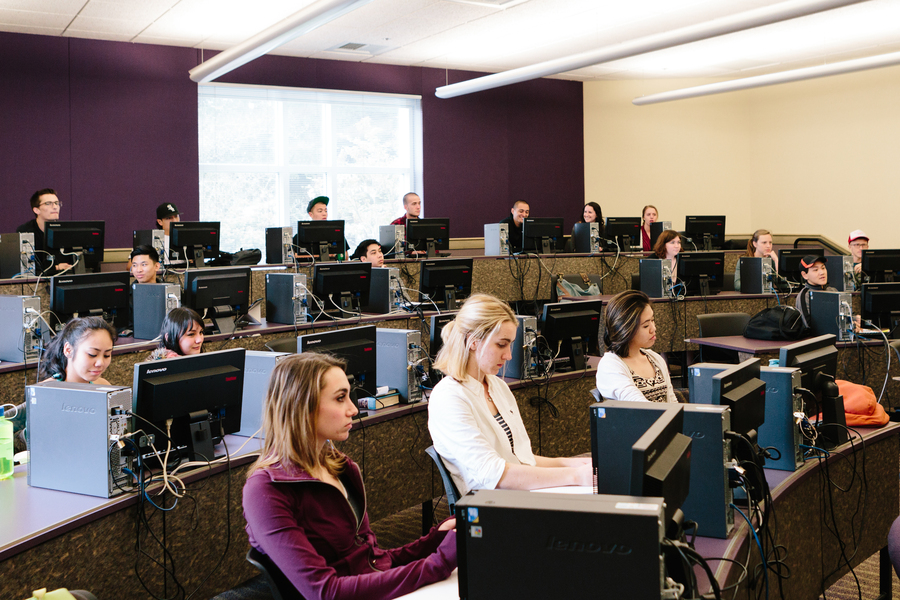 UP students in a management information systems course sit at desktop computers in a classroom with tiered seating during a lecture.