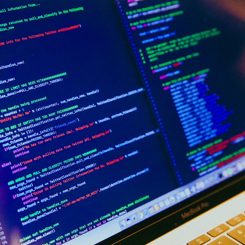 A close-up of a laptop screen displaying lines of colorful code in a dark setting.