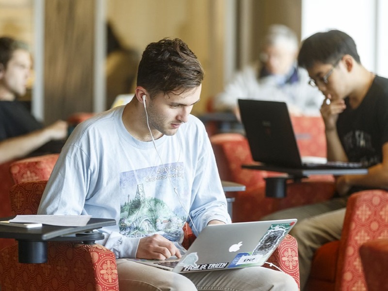 A student wearing headphones and sitting alone, looking at their laptop