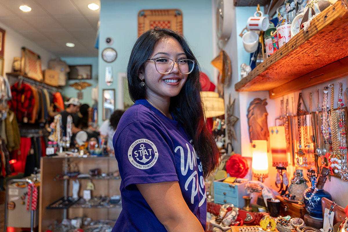 University of Portland student with glasses and long dark hair shops at a thrift store in Saint John's