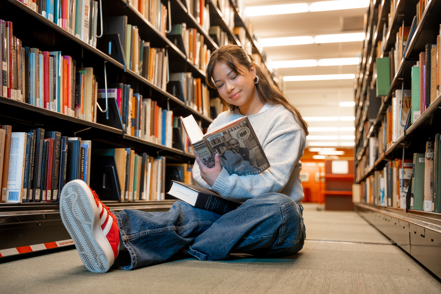 Student reading a book on the floor in the library