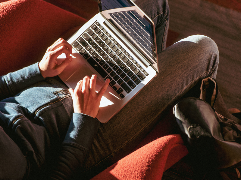 A close-up, above view of a UP student's hands using the mouse on an open laptop that's sitting on their legs.