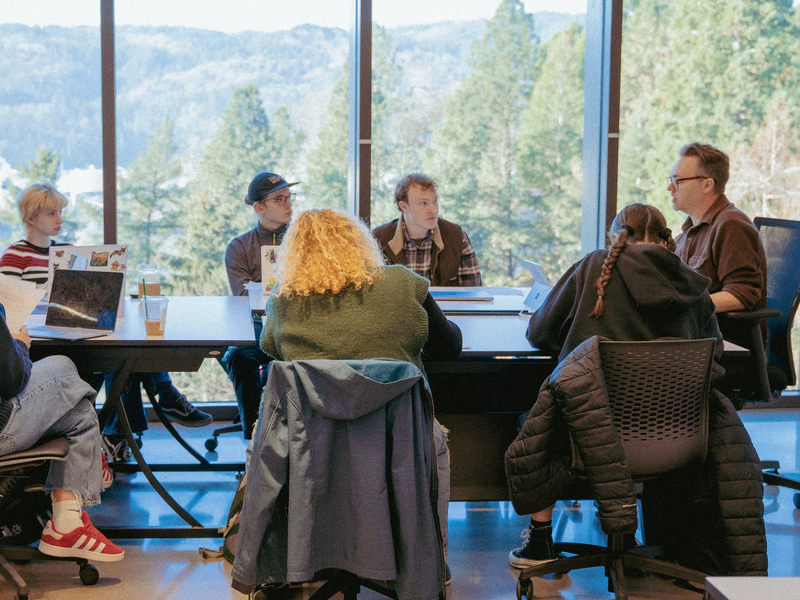 Students and a faculty member sit around a large table during an arts administration class with a mountain view behind them.