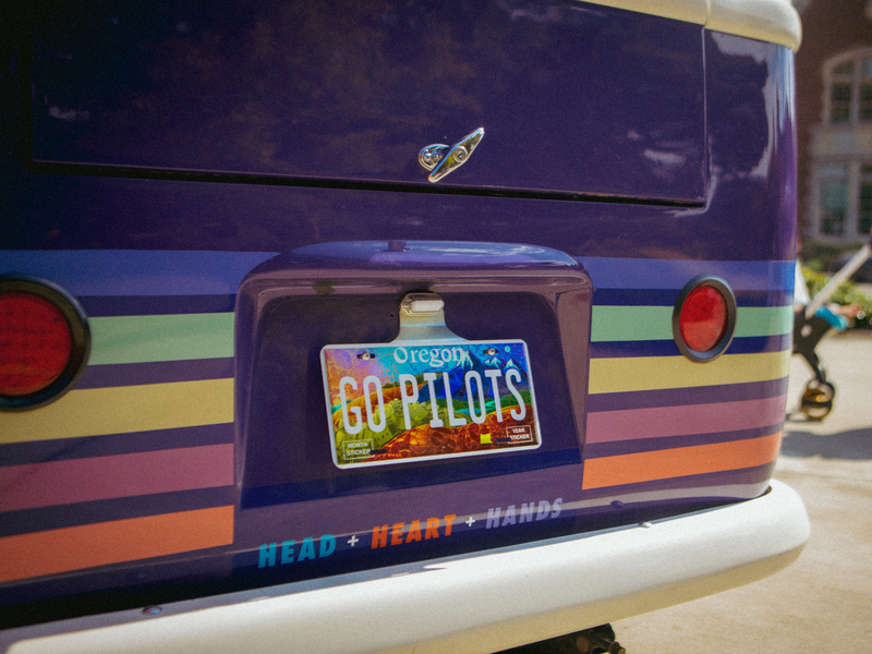 A close-up of a purple bus' Oregon license plate that reads "GO PILOTS."
