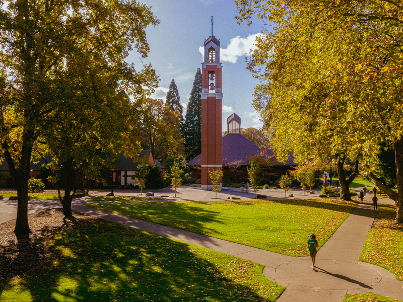University of Portland's bell tower on a sunny autumn day, surrounded by yellow and orange foliage.