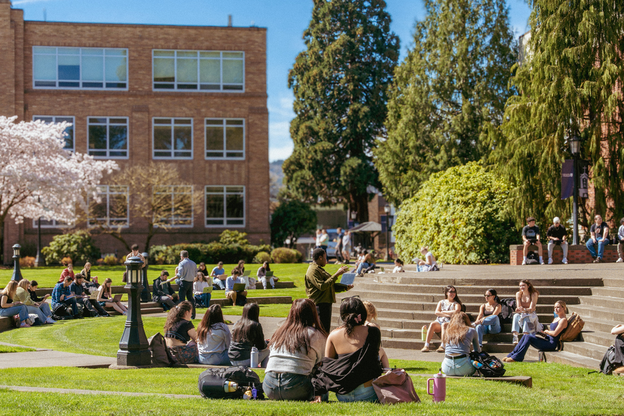 Multiple UP student groups sit in class clusters on the steps outside Fran Hall, listening to their professors speak.