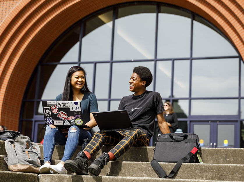 Two students work on their computers together while sitting on outdoor steps on University of Portland's campus