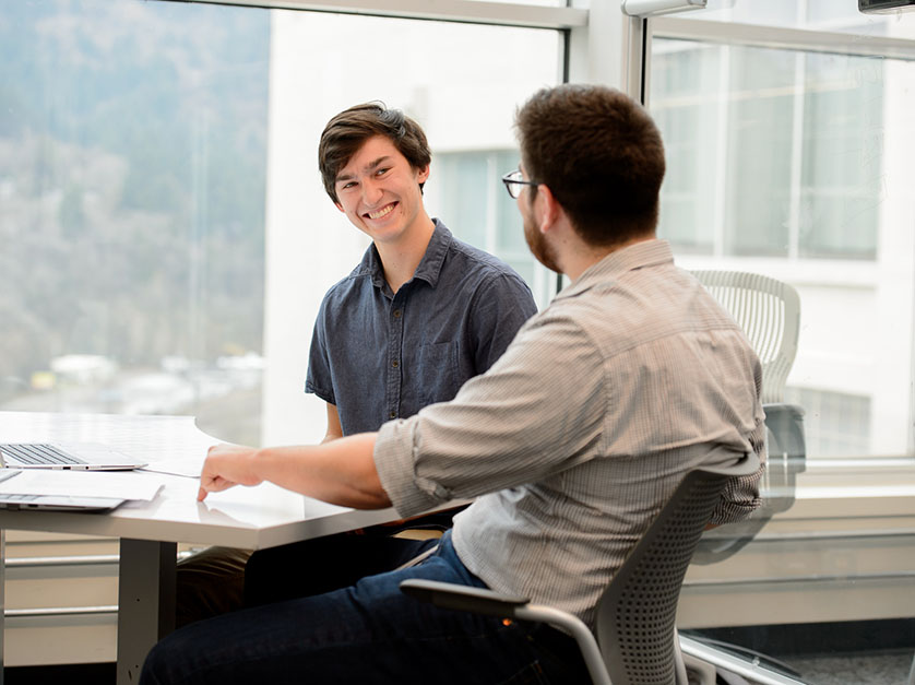 A student smiles while working with a professionally dressed man on a laptop