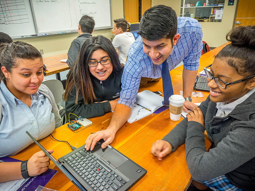 A professor leans across four students sitting at a table