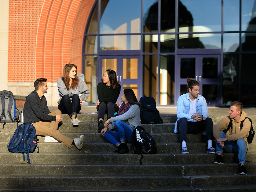 A group of students sit on the steps of a building while talking