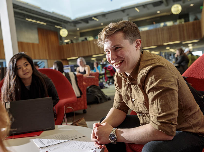 A student smiles while talking with friends in a common area