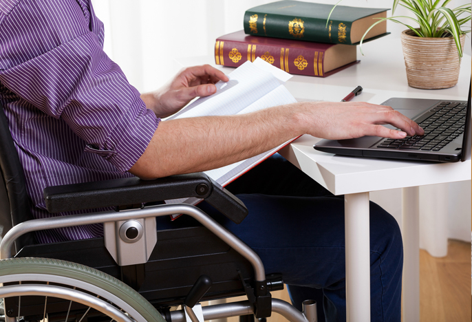 Student in wheelchair types on a laptop at a table.