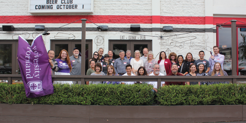 Alumni posing for a picture with the UP flag on a patio.