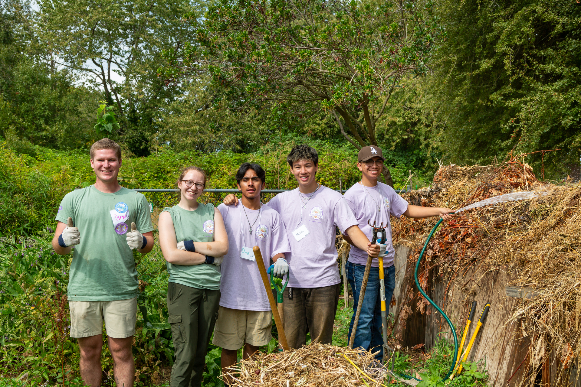 A group of UP students pose for a picture on a sunny day at the Fruits of Diversity community orchard during a volunteer service event.