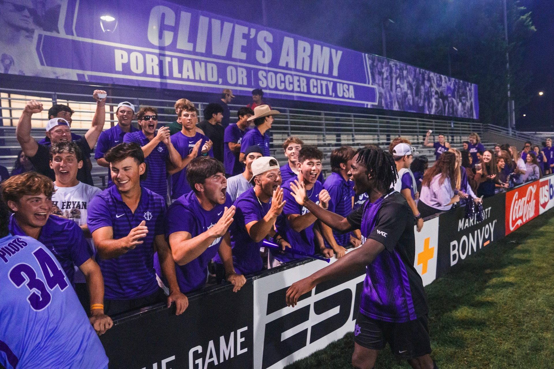 A member of the UP men's soccer team greets enthusiastic student fans during a game with hand shakes,