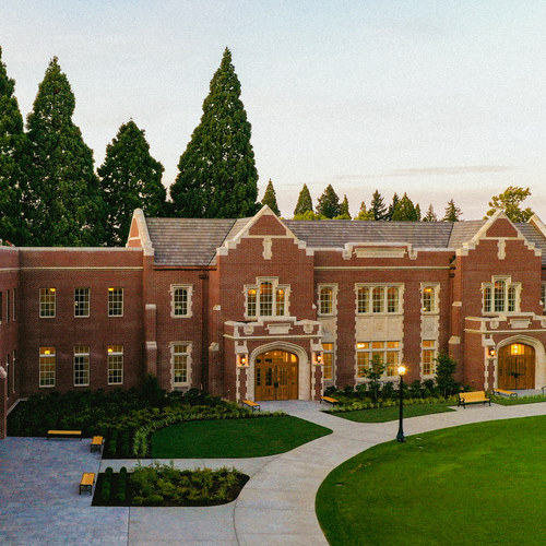 An exterior view of Dundon Berchtold Hall, a brick campus building with large windows and a manicured lawn.