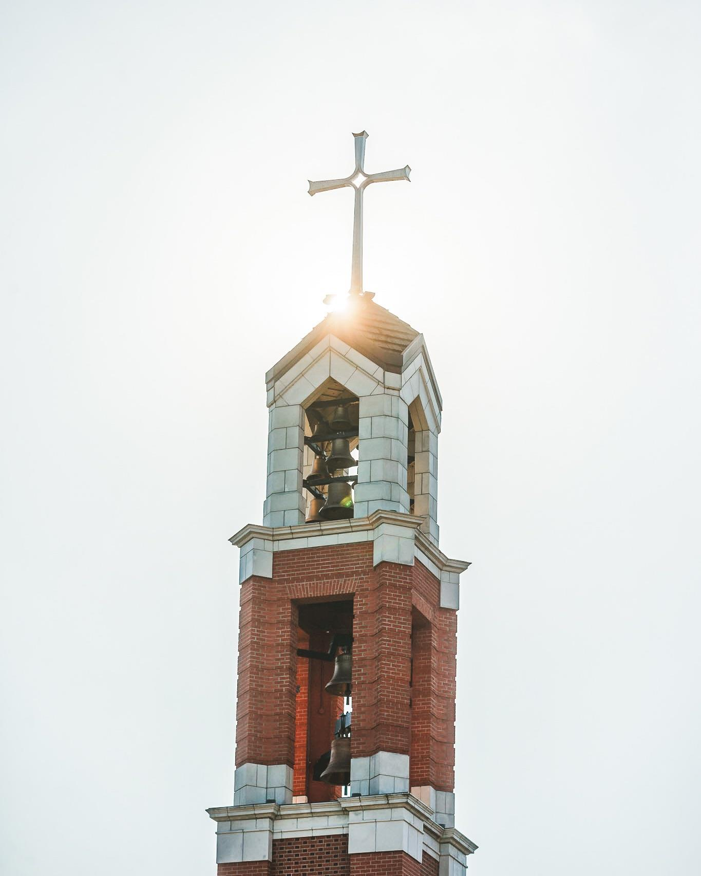 A spring view of the bell tower with the sun gleaming through the Cross.
