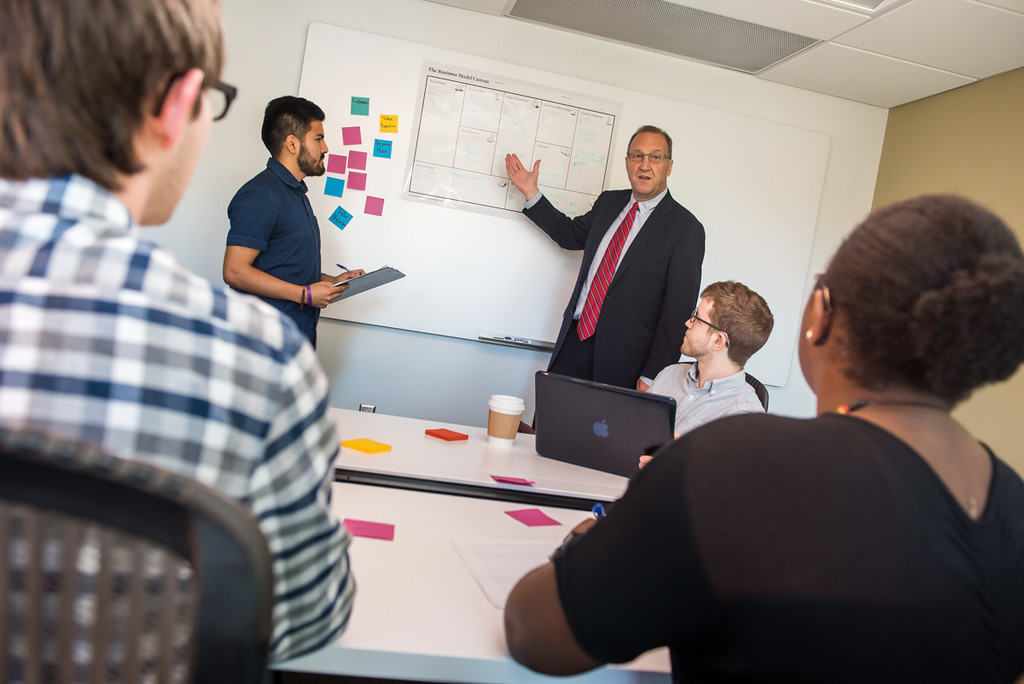 Small classroom setting with professor standing at the whiteboard