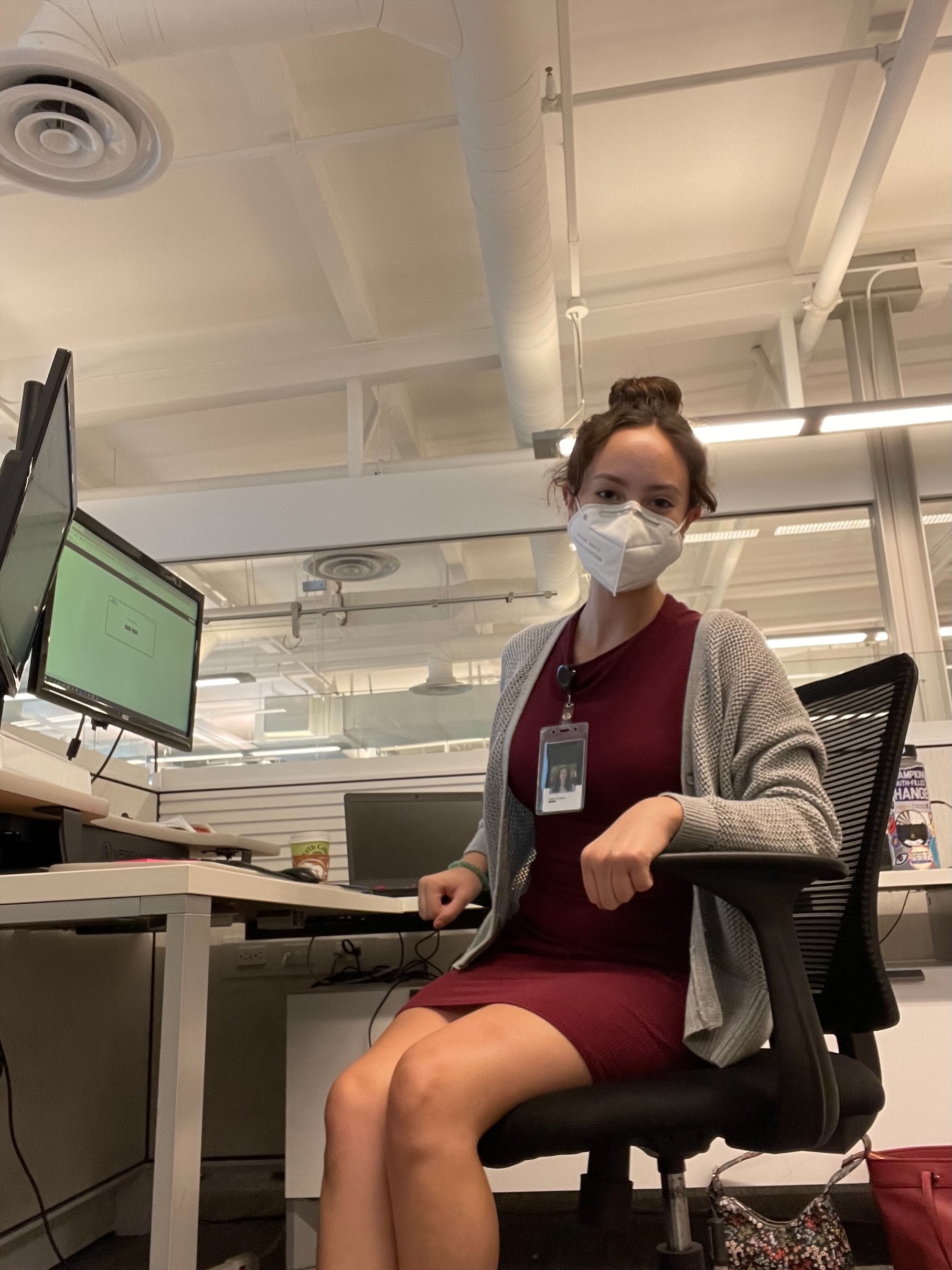 Photo of Isabel Cornejo sitting at a desk. She is wearing a face mask and an employee name badge. 